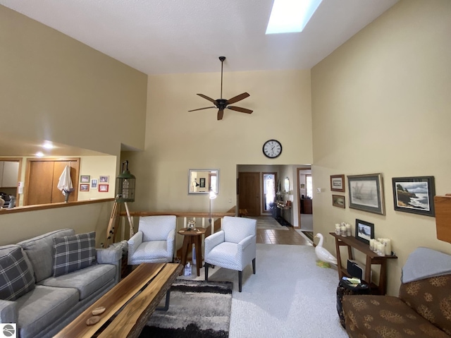 carpeted living room with ceiling fan, a skylight, and a towering ceiling