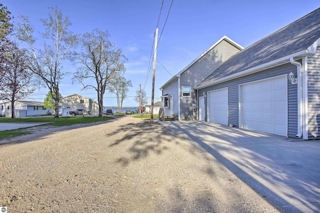 view of side of property with a residential view, an attached garage, driveway, and a shingled roof