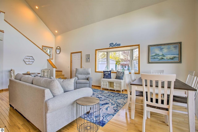 living room featuring light wood finished floors, high vaulted ceiling, stairs, and baseboards