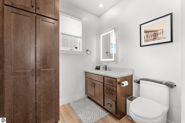 bathroom with recessed lighting, toilet, vanity, wood finished floors, and baseboards