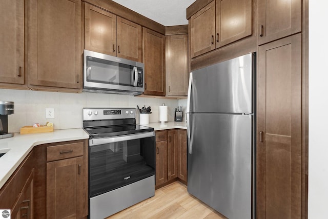 kitchen featuring light countertops, appliances with stainless steel finishes, backsplash, and light wood-style floors