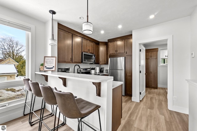 kitchen with appliances with stainless steel finishes, a breakfast bar area, a peninsula, light countertops, and light wood-type flooring