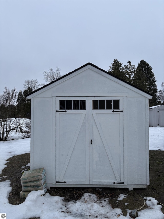 snow covered structure featuring a storage shed and an outbuilding