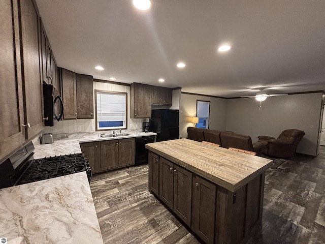 kitchen with dark wood-style floors, butcher block counters, dark brown cabinets, black appliances, and a sink