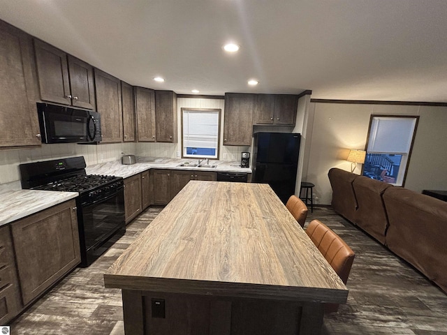 kitchen featuring dark brown cabinetry, black appliances, open floor plan, and a sink