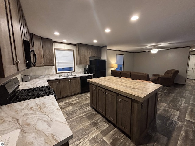 kitchen with a kitchen island, a sink, dark brown cabinets, dark wood-style floors, and black appliances