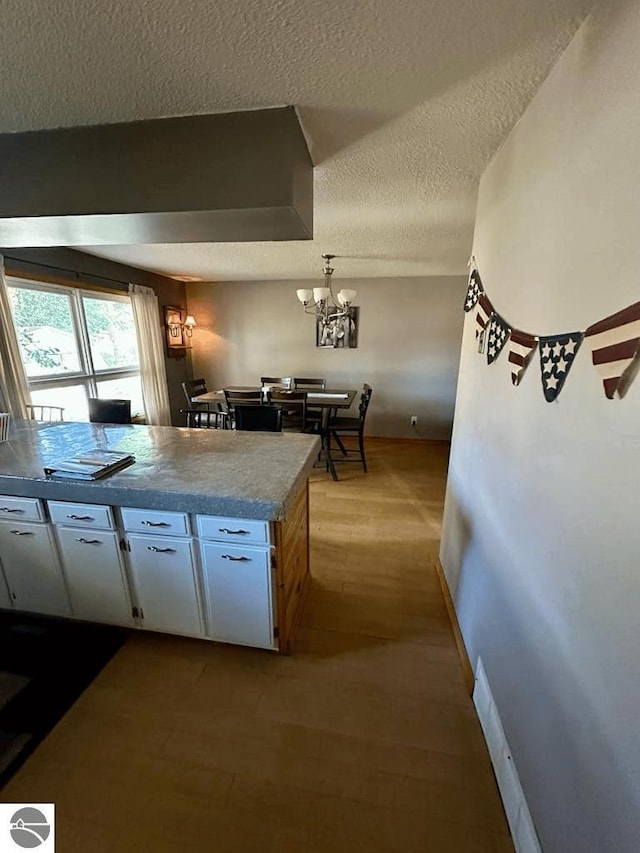 kitchen with baseboards, wood finished floors, a textured ceiling, white cabinetry, and a notable chandelier