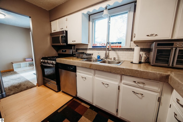 kitchen featuring light wood finished floors, tasteful backsplash, appliances with stainless steel finishes, white cabinets, and a sink