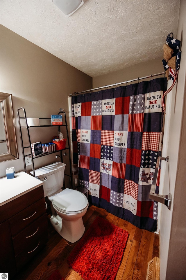 full bathroom with a textured ceiling, curtained shower, toilet, wood finished floors, and vanity