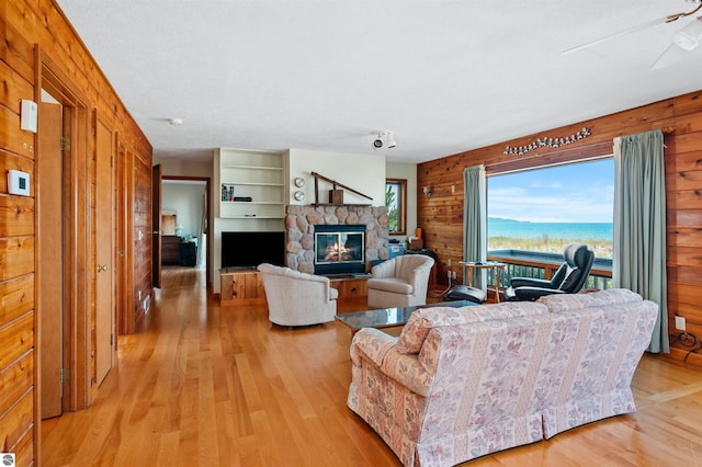 living area with light wood-type flooring, wood walls, and a stone fireplace