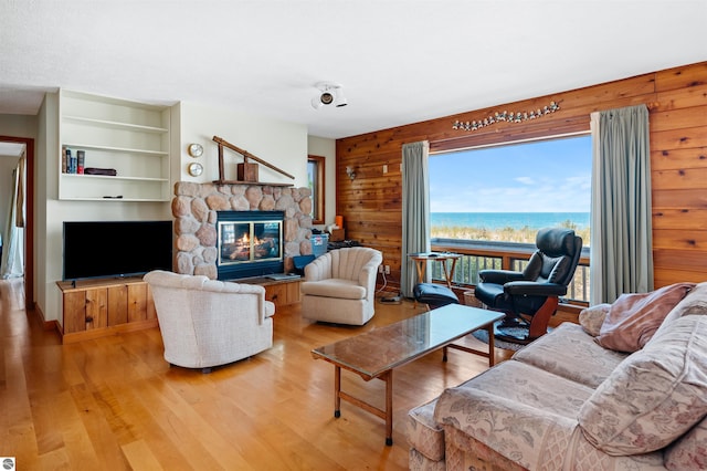 living area featuring light wood-style flooring, wood walls, a water view, a fireplace, and built in features