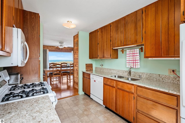 kitchen with white appliances, brown cabinetry, a sink, and a ceiling fan