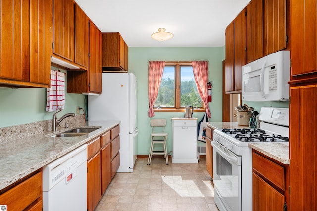 kitchen with white appliances, brown cabinetry, a sink, and baseboards