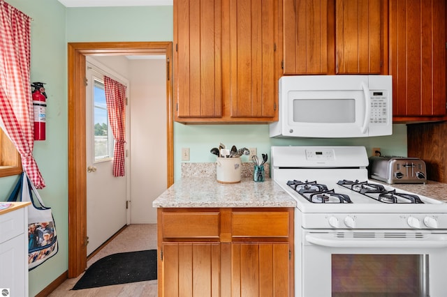 kitchen with white appliances, brown cabinets, and light stone countertops