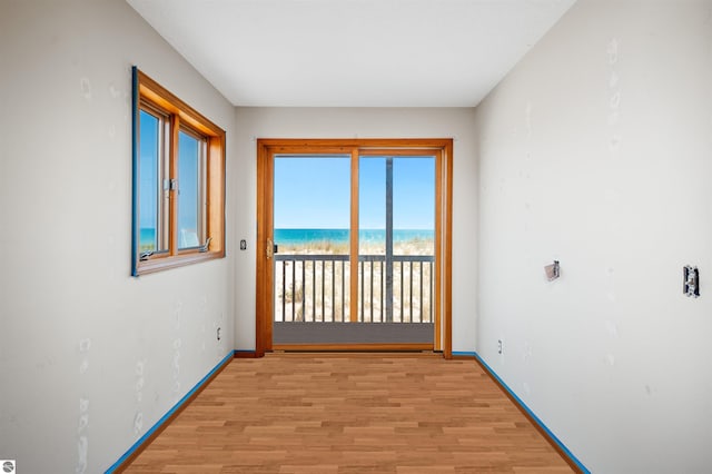 spare room with light wood-type flooring, a water view, and baseboards