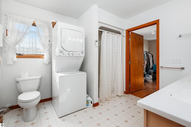 full bath with stacked washer and dryer, toilet, vanity, baseboards, and tile patterned floors