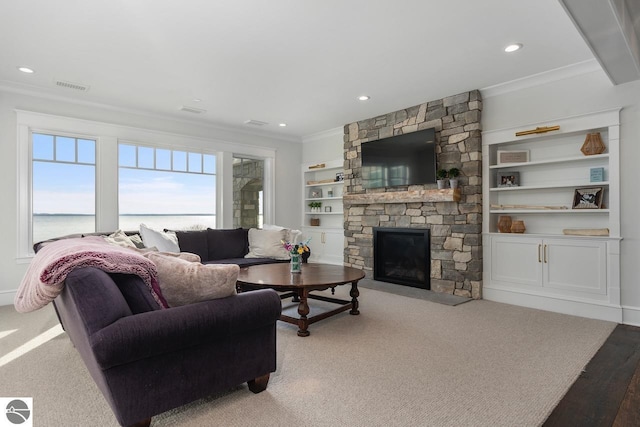 carpeted living area with built in features, visible vents, recessed lighting, ornamental molding, and a stone fireplace