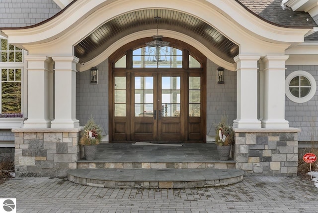 view of exterior entry featuring french doors, stone siding, roof with shingles, and a porch