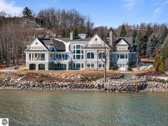 rear view of property featuring stone siding, a water view, and a balcony