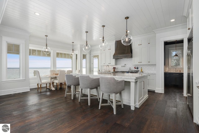 kitchen with tasteful backsplash, an island with sink, wall chimney exhaust hood, and ornamental molding