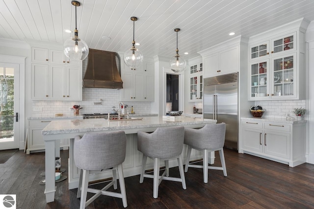 kitchen with dark wood-style floors, built in fridge, white cabinetry, glass insert cabinets, and custom exhaust hood