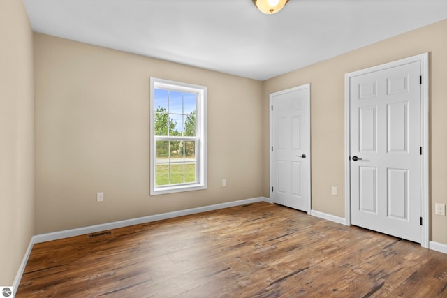 unfurnished bedroom with wood finished floors, visible vents, and baseboards