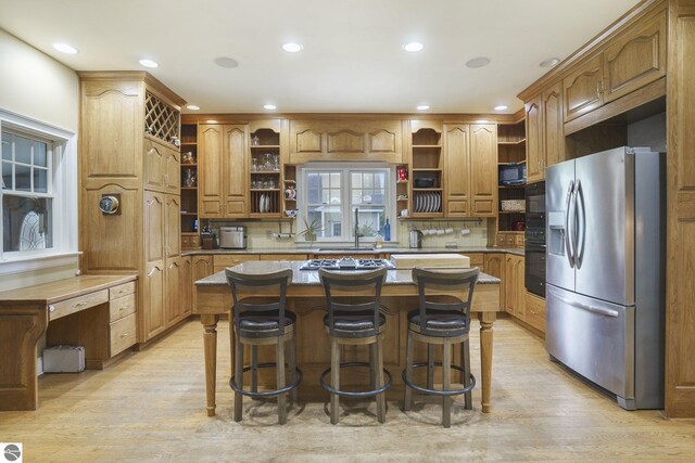 kitchen featuring a kitchen island, open shelves, light wood-style flooring, a kitchen breakfast bar, and stainless steel fridge