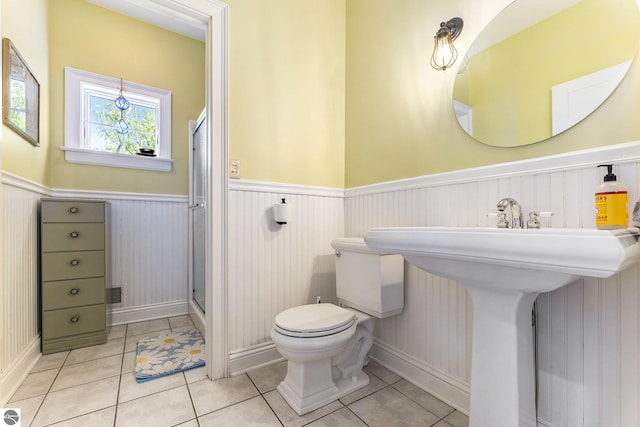 bathroom featuring tile patterned flooring, a shower stall, toilet, and wainscoting