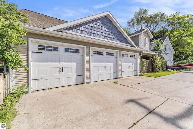 view of side of home with an attached garage, driveway, and a shingled roof