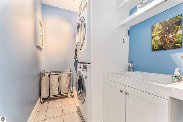 laundry area with baseboards, light tile patterned floors, stacked washer and clothes dryer, cabinet space, and a sink