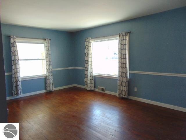 empty room with wood finished floors, visible vents, and baseboards