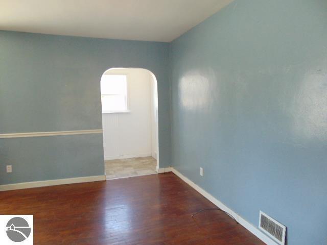 unfurnished room with visible vents, arched walkways, baseboards, and wood finished floors