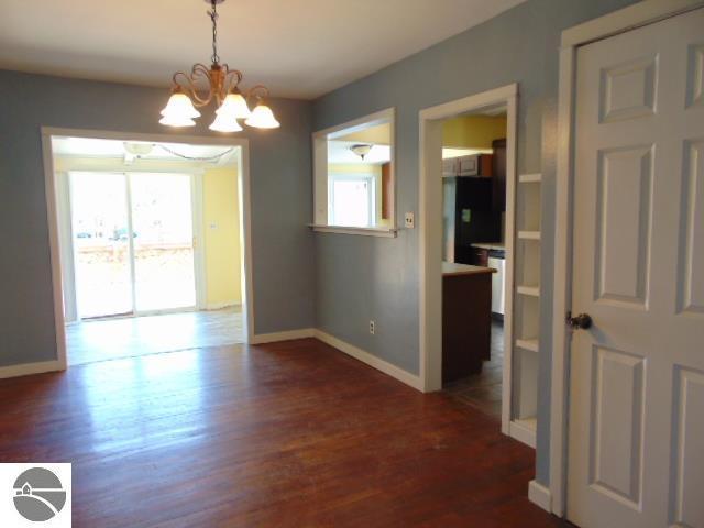 unfurnished dining area with a notable chandelier, dark wood-type flooring, and baseboards