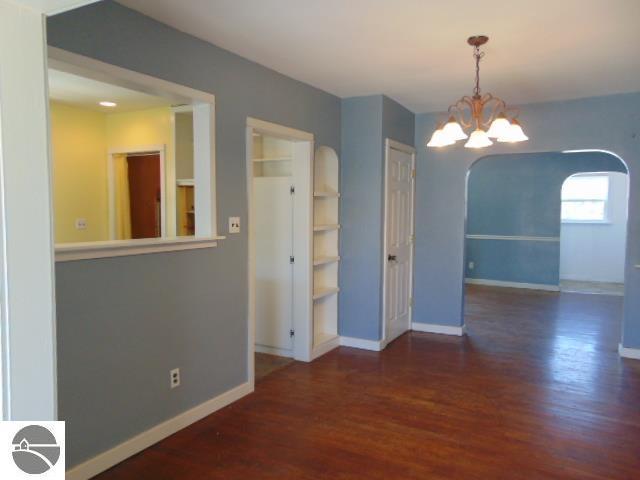 unfurnished dining area featuring baseboards, arched walkways, a notable chandelier, and wood finished floors