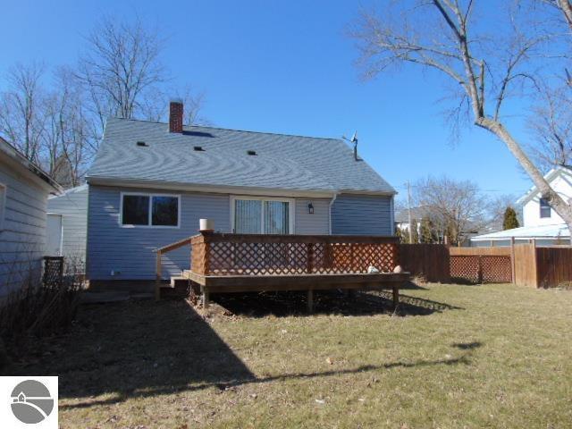 rear view of house with a chimney, a wooden deck, a yard, and fence