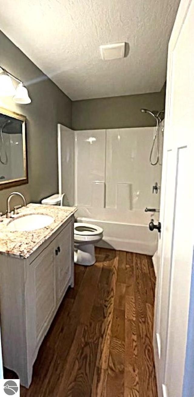 bathroom with toilet, a textured ceiling, wood finished floors, shower / bathing tub combination, and vanity