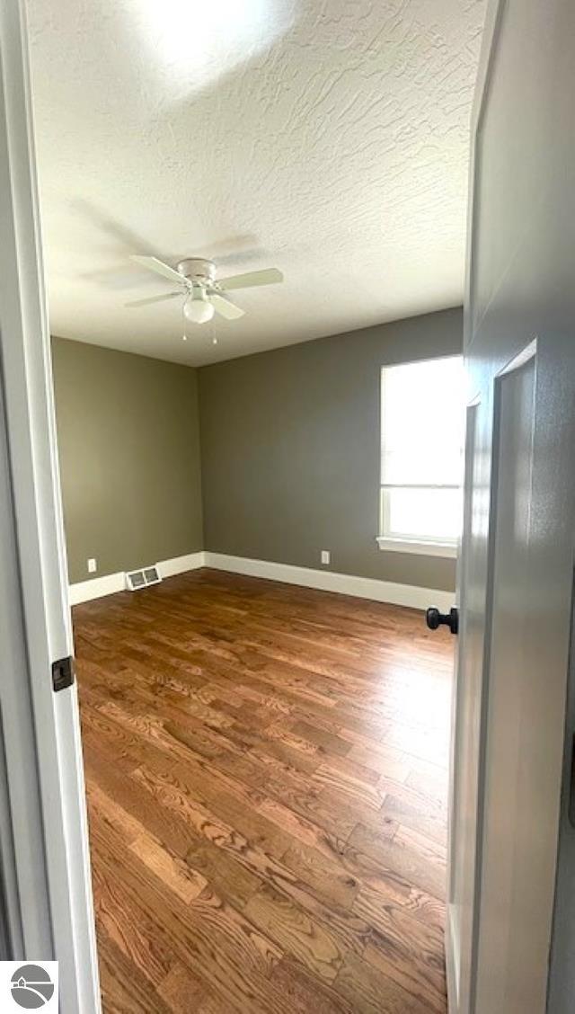 spare room featuring visible vents, a textured ceiling, baseboards, ceiling fan, and dark wood-style flooring