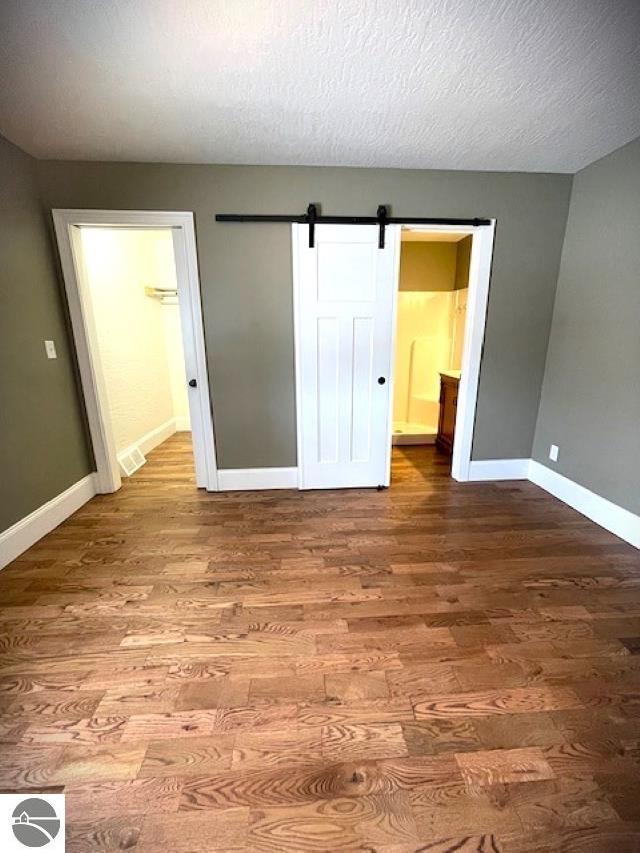 unfurnished bedroom featuring visible vents, baseboards, a barn door, and wood finished floors