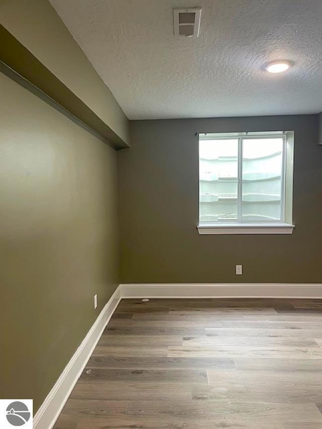 empty room with visible vents, a textured ceiling, baseboards, and wood finished floors