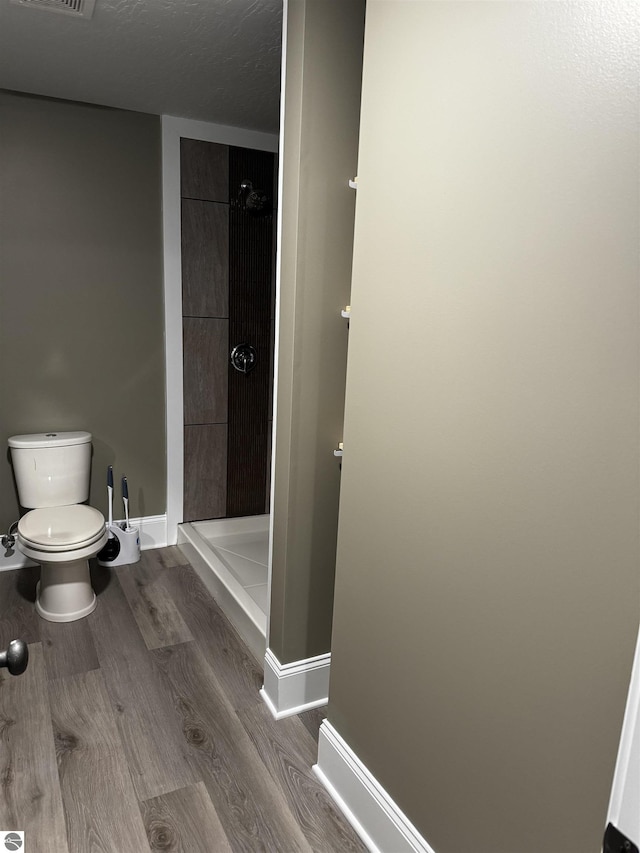 bathroom featuring visible vents, toilet, wood finished floors, a shower stall, and baseboards