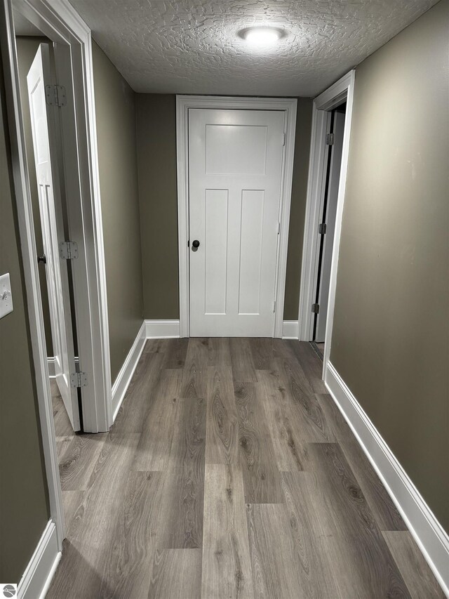 hallway with baseboards, a textured ceiling, and wood finished floors