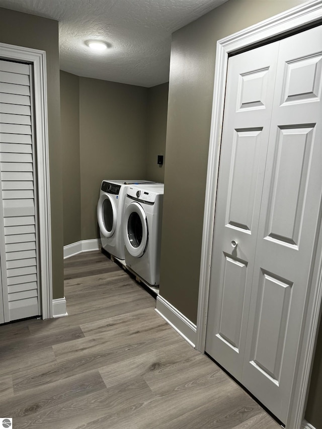 laundry area with wood finished floors, baseboards, laundry area, a textured ceiling, and washer and clothes dryer