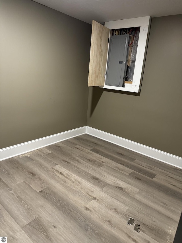 spare room with electric panel, baseboards, and wood finished floors