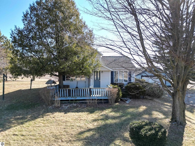 exterior space with a wooden deck, a front yard, and roof with shingles