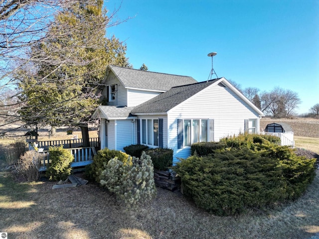 view of side of home featuring a wooden deck and a shingled roof