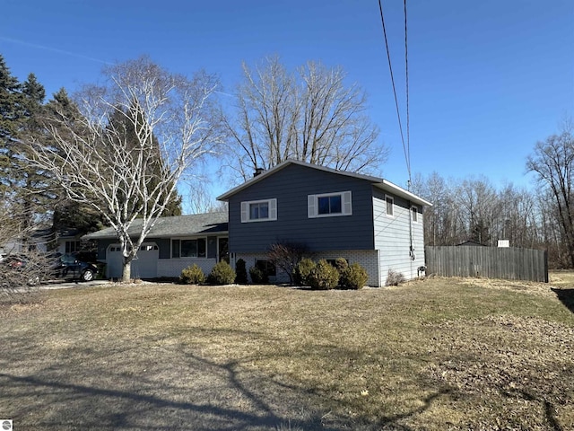 tri-level home with a garage, brick siding, a front lawn, and fence