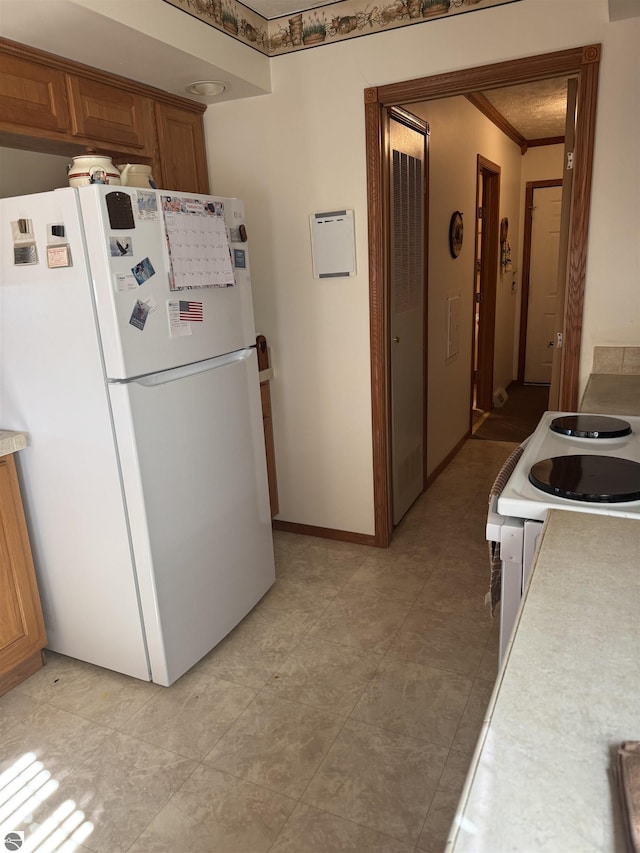 kitchen featuring brown cabinetry, baseboards, freestanding refrigerator, light countertops, and crown molding