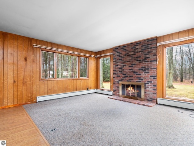 unfurnished living room with a baseboard heating unit, wooden walls, wood finished floors, and a fireplace