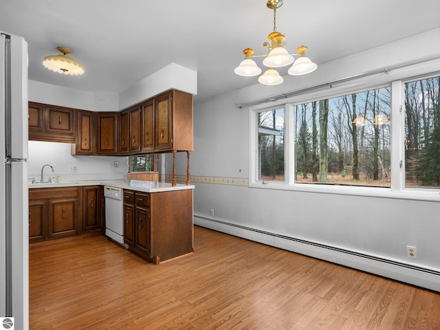 kitchen featuring white appliances, a baseboard radiator, light wood-style flooring, a sink, and light countertops