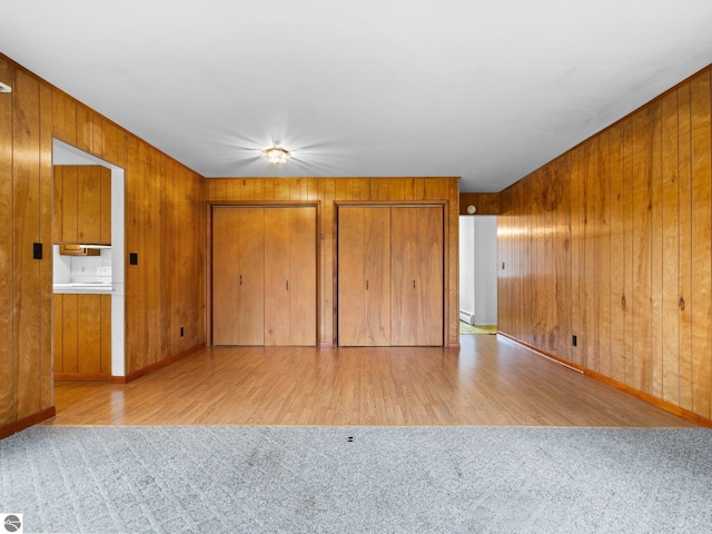 unfurnished bedroom featuring wooden walls, wood finished floors, and two closets